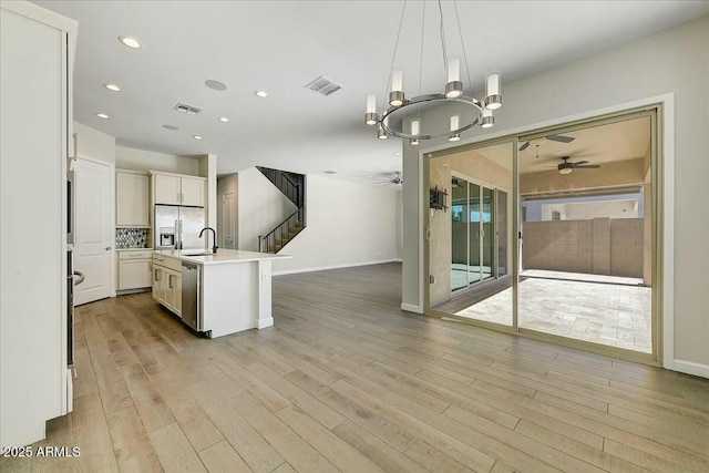 kitchen featuring sink, hanging light fixtures, a center island with sink, appliances with stainless steel finishes, and ceiling fan with notable chandelier