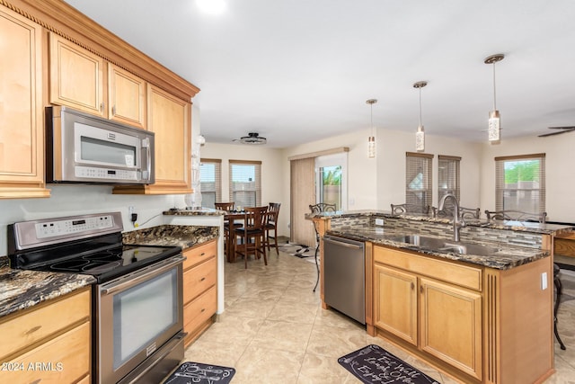 kitchen with a breakfast bar, sink, hanging light fixtures, dark stone countertops, and appliances with stainless steel finishes