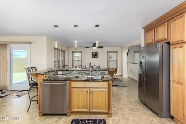 kitchen featuring sink, decorative light fixtures, dark stone counters, an island with sink, and stainless steel appliances