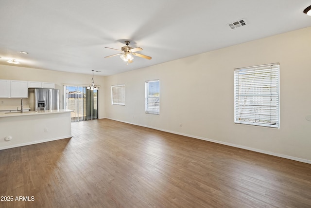 unfurnished living room featuring visible vents, a sink, ceiling fan with notable chandelier, and wood finished floors