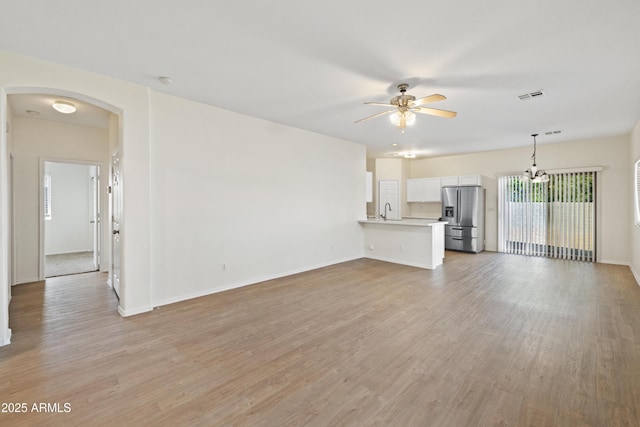 unfurnished living room with arched walkways, visible vents, light wood finished floors, and ceiling fan with notable chandelier