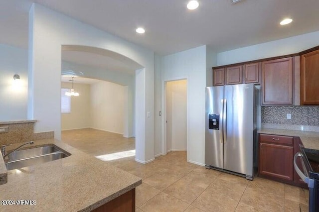 kitchen featuring sink, backsplash, a notable chandelier, light stone counters, and stainless steel appliances