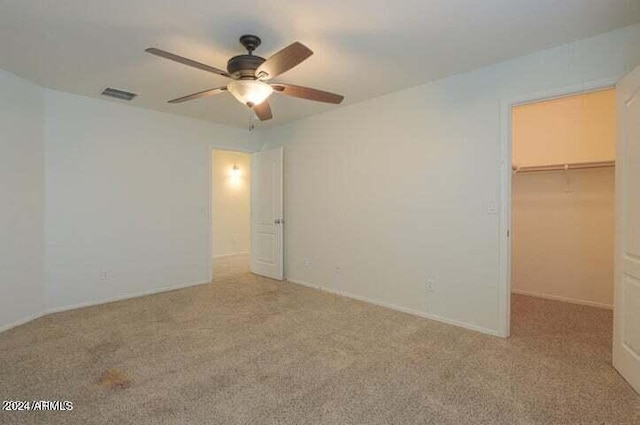 unfurnished bedroom with a walk in closet, light colored carpet, ceiling fan, and a closet