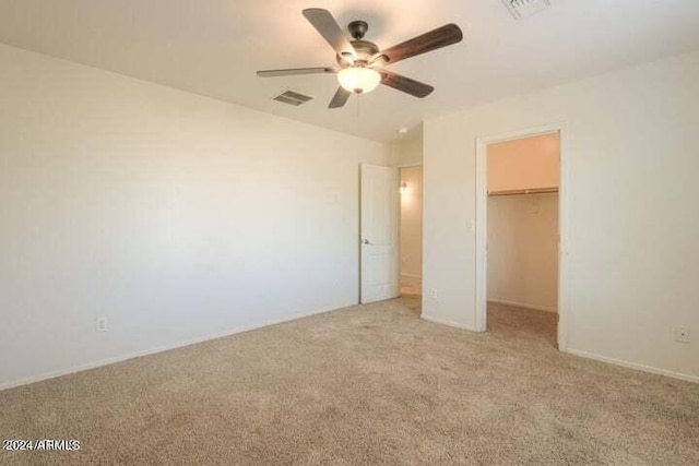 unfurnished bedroom with a walk in closet, light carpet, ceiling fan, and a closet