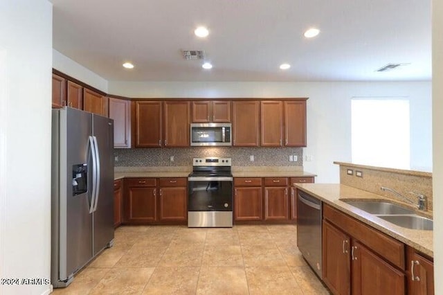 kitchen with tasteful backsplash, appliances with stainless steel finishes, light stone countertops, and sink