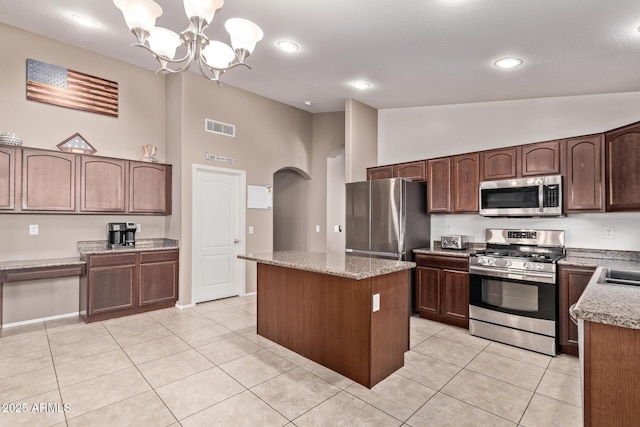 kitchen with arched walkways, light tile patterned floors, a kitchen island, visible vents, and appliances with stainless steel finishes