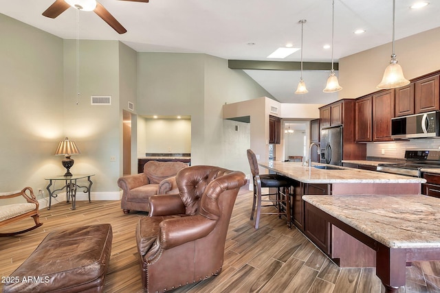 kitchen featuring a kitchen breakfast bar, stainless steel appliances, a large island with sink, and light stone counters