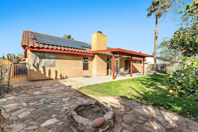 rear view of house featuring solar panels, a patio area, and a lawn