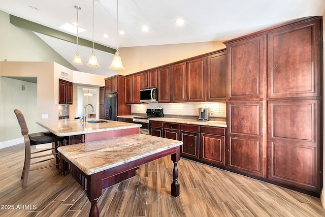 kitchen featuring hanging light fixtures, light stone counters, appliances with stainless steel finishes, a kitchen breakfast bar, and decorative backsplash