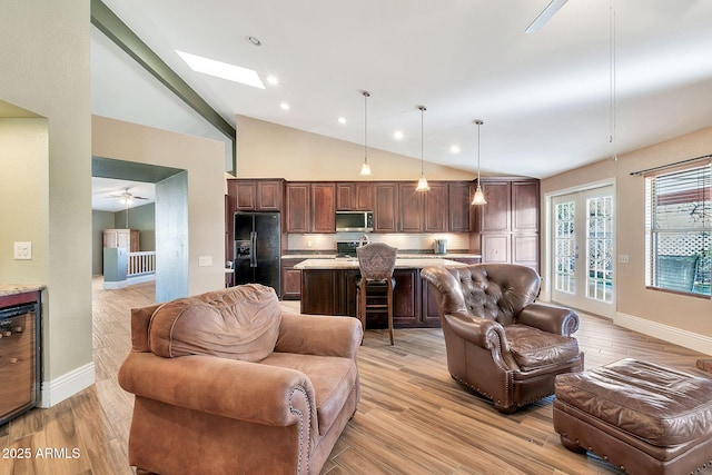 living room with light wood-type flooring, high vaulted ceiling, ceiling fan, and a skylight