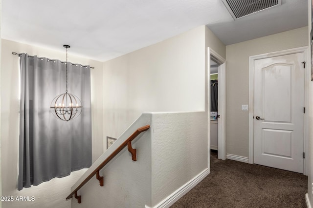 hall featuring an inviting chandelier and dark colored carpet