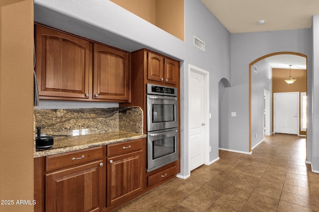 11101 W Wilshire Dr, Avondale, AZ 85392 - kitchen featuring stainless steel double oven, arched walkways, brown cabinetry, baseboards, and a towering ceiling
