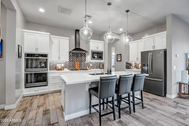 kitchen featuring appliances with stainless steel finishes, pendant lighting, white cabinetry, and wall chimney exhaust hood