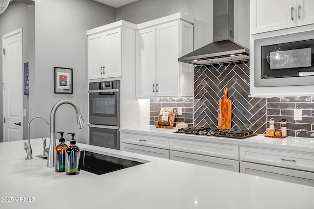 kitchen with sink, stainless steel appliances, wall chimney range hood, decorative backsplash, and white cabinets