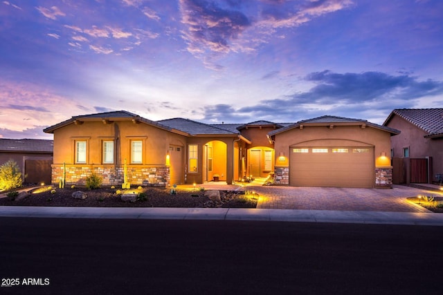 view of front of home featuring a garage, stone siding, fence, decorative driveway, and stucco siding