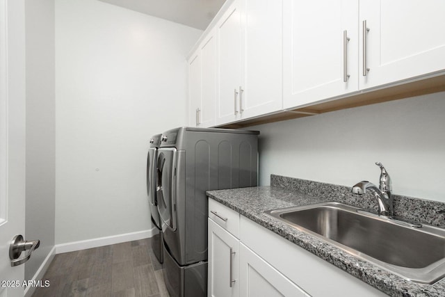 clothes washing area featuring wood finished floors, a sink, baseboards, independent washer and dryer, and cabinet space