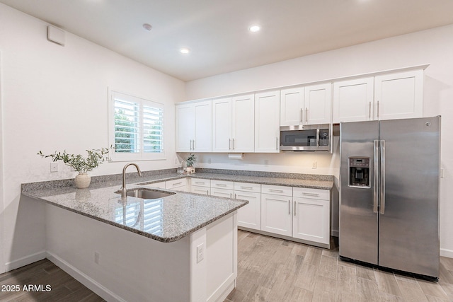 kitchen featuring light stone countertops, light wood-style flooring, appliances with stainless steel finishes, and a sink