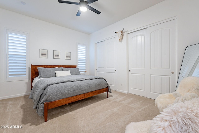 bedroom featuring multiple closets, light colored carpet, ceiling fan, and baseboards