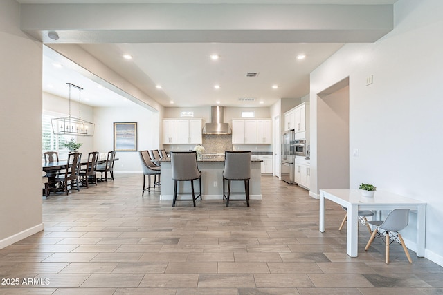 kitchen with wall chimney exhaust hood, visible vents, decorative backsplash, white cabinets, and a kitchen breakfast bar