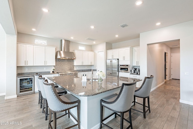 kitchen with wine cooler, visible vents, a kitchen breakfast bar, wall chimney range hood, and appliances with stainless steel finishes