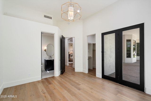 unfurnished bedroom with ensuite bath, a chandelier, a spacious closet, light wood-type flooring, and visible vents