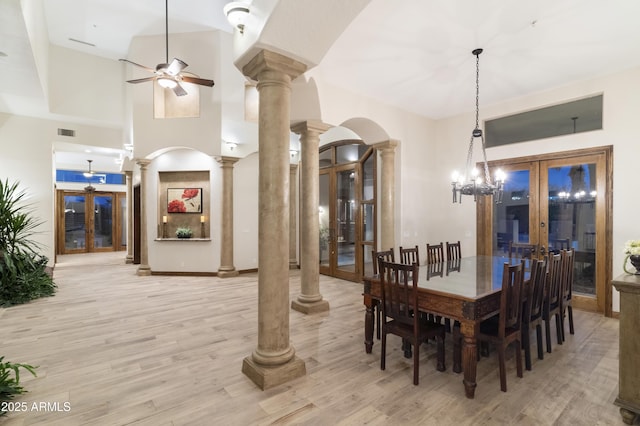 dining room with a towering ceiling, decorative columns, ceiling fan, light hardwood / wood-style floors, and french doors