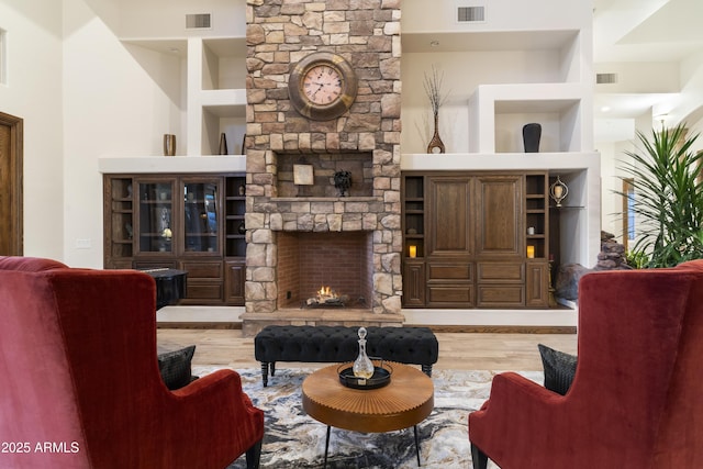 living room with built in shelves, a stone fireplace, and light hardwood / wood-style flooring