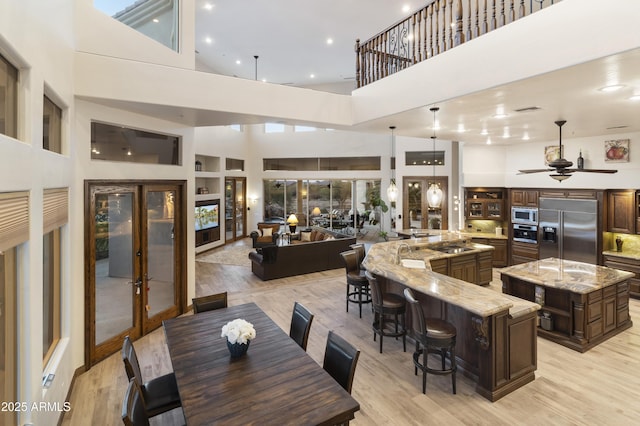 dining room with ceiling fan, a towering ceiling, light hardwood / wood-style floors, and french doors