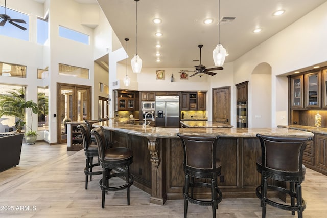 bar with ceiling fan, hanging light fixtures, a towering ceiling, dark brown cabinets, and built in appliances