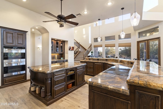 kitchen featuring double oven, dark stone counters, hanging light fixtures, dark brown cabinets, and black electric cooktop