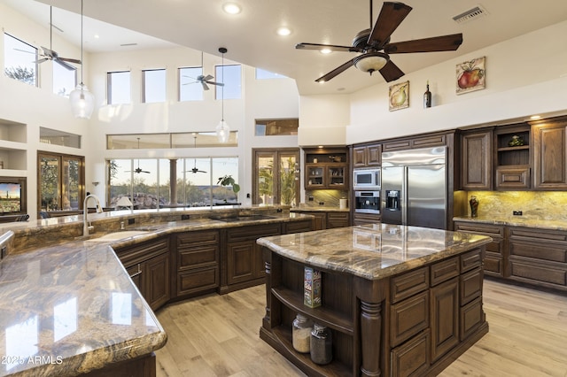 kitchen with built in appliances, decorative light fixtures, dark stone counters, a large island, and a high ceiling