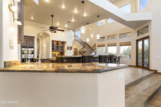 kitchen featuring dark stone counters, decorative light fixtures, kitchen peninsula, and a high ceiling