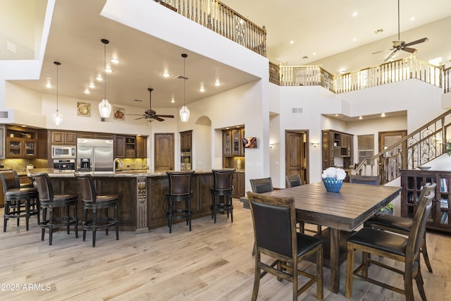 dining area featuring a high ceiling, ceiling fan, and light hardwood / wood-style floors