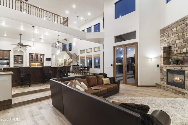 living room featuring a high ceiling, ceiling fan, a stone fireplace, and light hardwood / wood-style floors