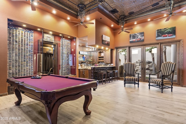 game room featuring pool table, a towering ceiling, light hardwood / wood-style floors, and bar area