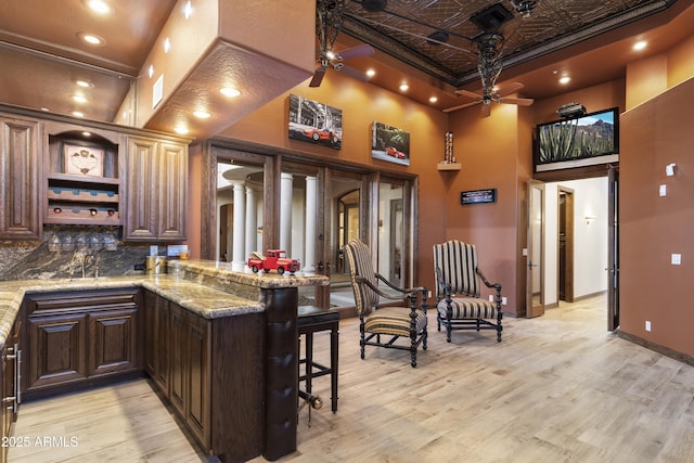 bar with tasteful backsplash, light stone countertops, light hardwood / wood-style floors, and a high ceiling