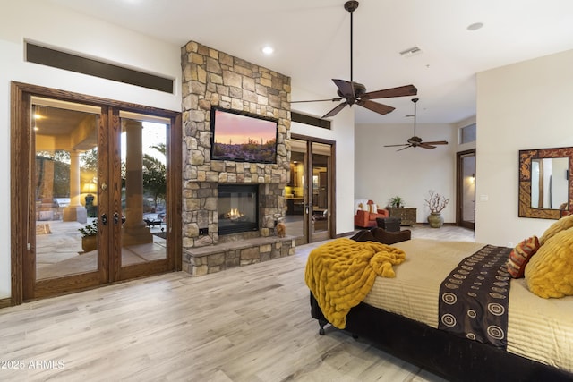 bedroom featuring access to exterior, a stone fireplace, light hardwood / wood-style floors, and french doors