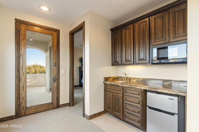 kitchen with sink, dark brown cabinets, light carpet, stainless steel refrigerator, and dark stone counters