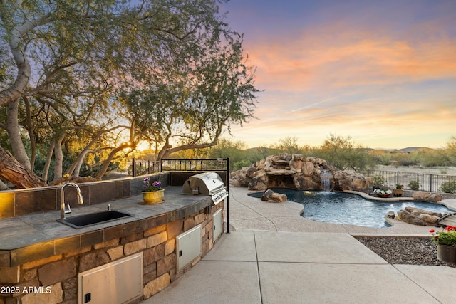 patio terrace at dusk featuring sink, a fenced in pool, area for grilling, pool water feature, and exterior kitchen