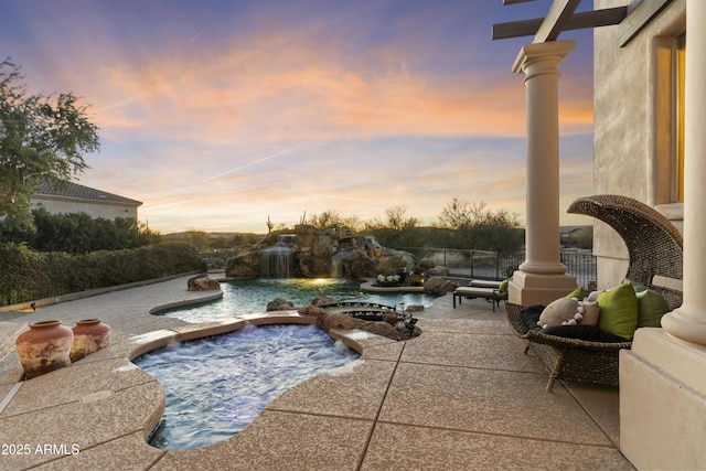 pool at dusk featuring a patio, pool water feature, and an in ground hot tub