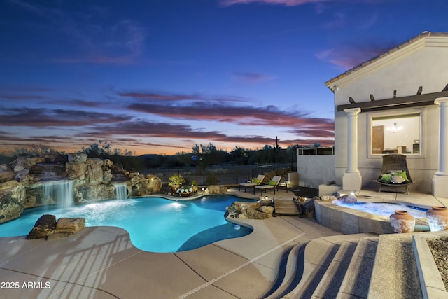 pool at dusk with an in ground hot tub, pool water feature, and a patio