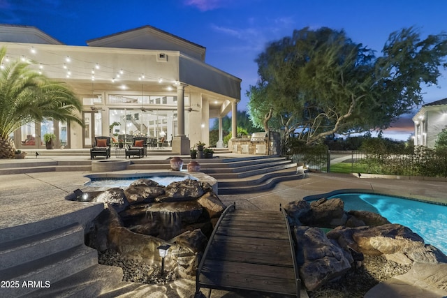 pool at dusk with a patio area, ceiling fan, and exterior kitchen