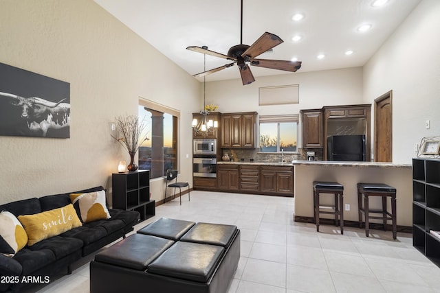 living room with ceiling fan with notable chandelier, light tile patterned flooring, sink, and a high ceiling