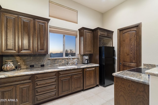 kitchen with black refrigerator, sink, decorative backsplash, and stone counters