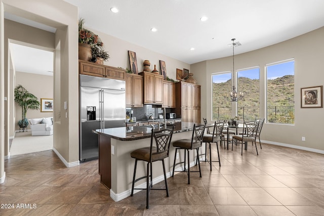 kitchen featuring built in refrigerator, pendant lighting, decorative backsplash, a kitchen breakfast bar, and dark stone countertops