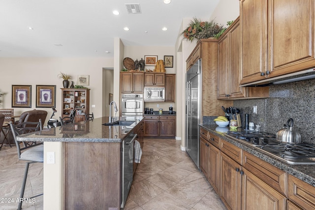 kitchen featuring a kitchen island with sink, built in appliances, sink, and a breakfast bar