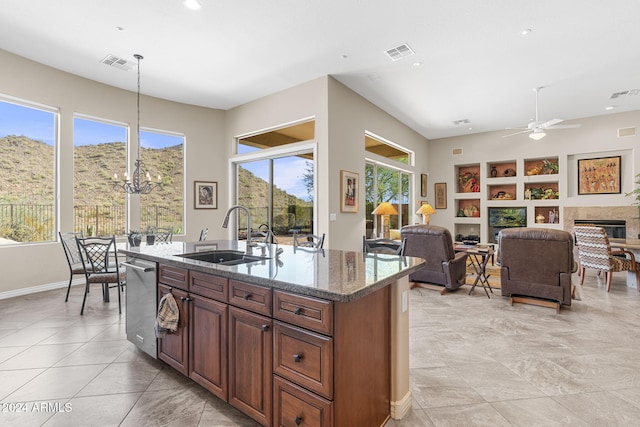 kitchen with sink, ceiling fan, dark stone countertops, an island with sink, and pendant lighting