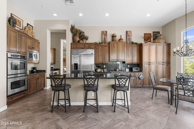 kitchen featuring built in appliances, a kitchen breakfast bar, a center island with sink, and an inviting chandelier