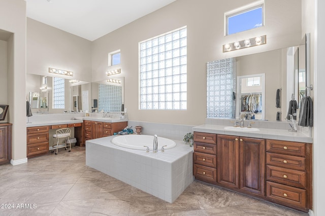 bathroom with vanity, a towering ceiling, tile patterned flooring, and tiled tub