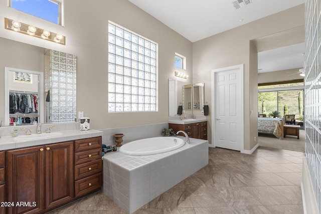 bathroom with a relaxing tiled tub, vanity, and tile patterned floors